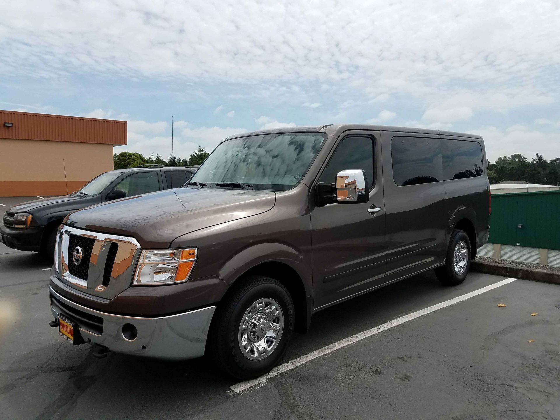 Brown Nissan passenger van parked in a lot under a partly cloudy sky.