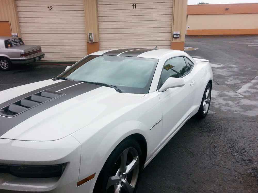 White Chevy Camaro with black racing stripes parked in front of garage doors.