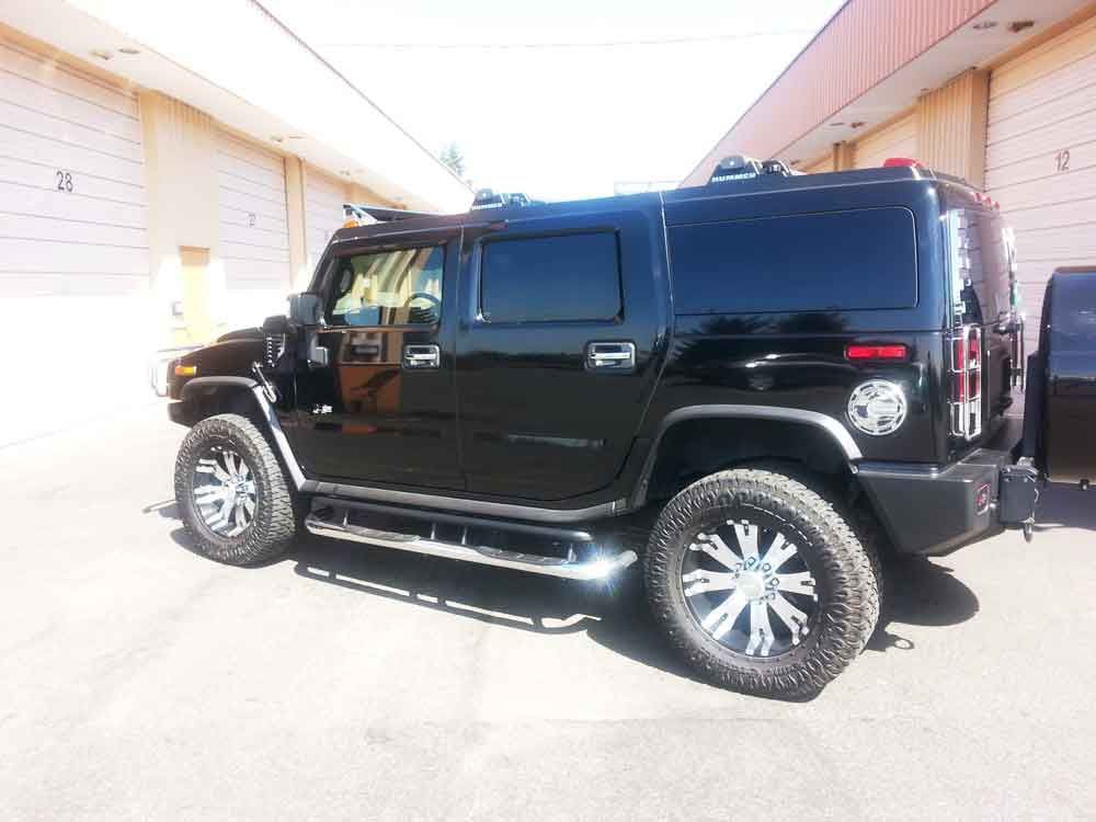 Black Hummer H2 SUV with chrome accents and custom wheels parked in front of industrial building.