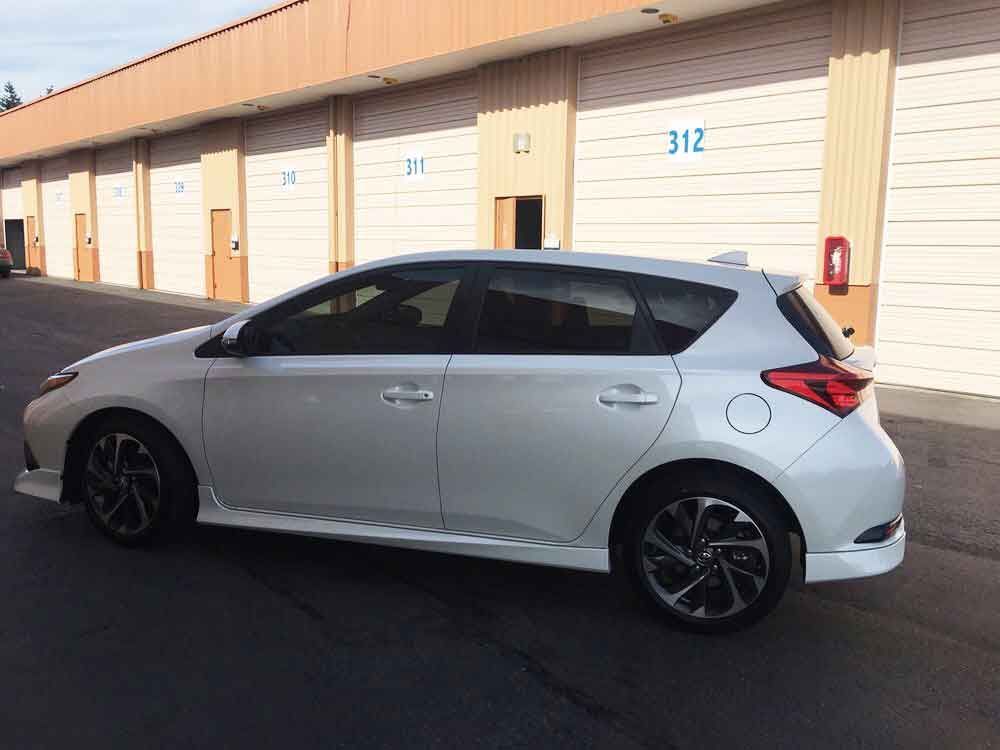 White hatchback car parked in front of tan storage units.