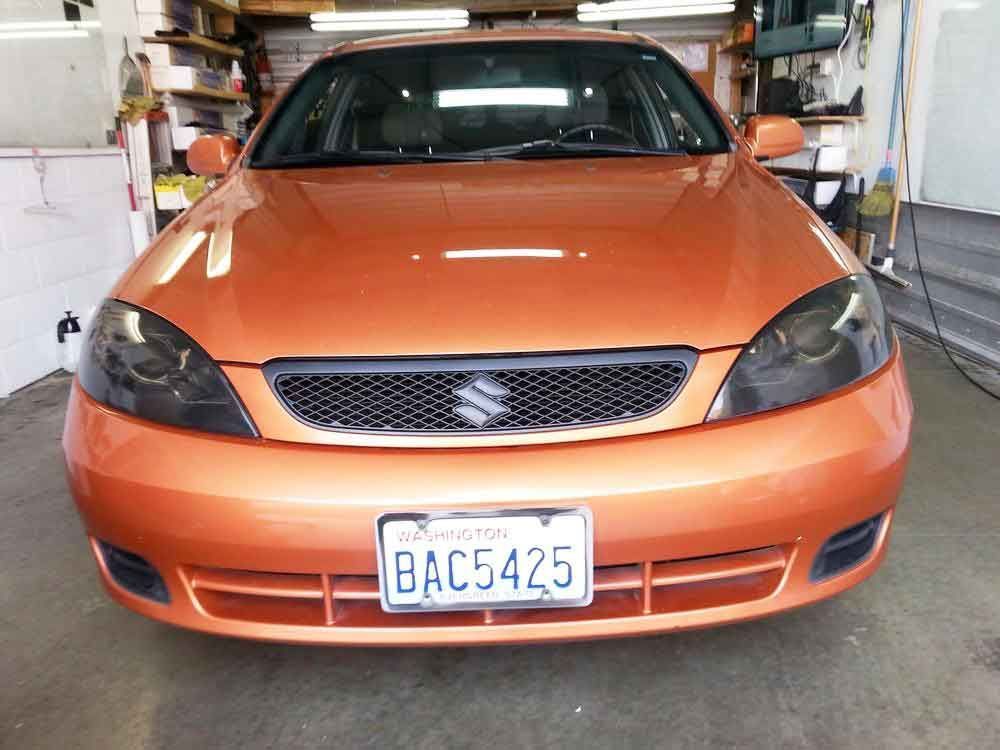 Orange Suzuki sedan with blacked-out headlights, California license plate BAC5425, parked indoors.