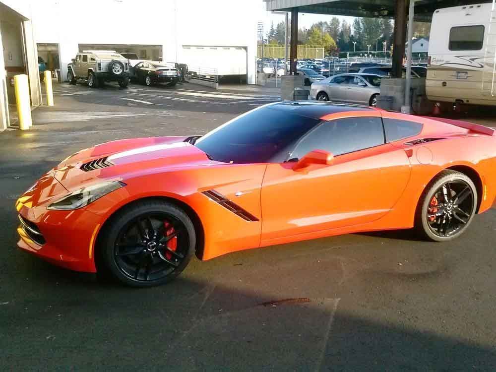 Bright orange Corvette parked outside a garage, black wheels, tinted windows.