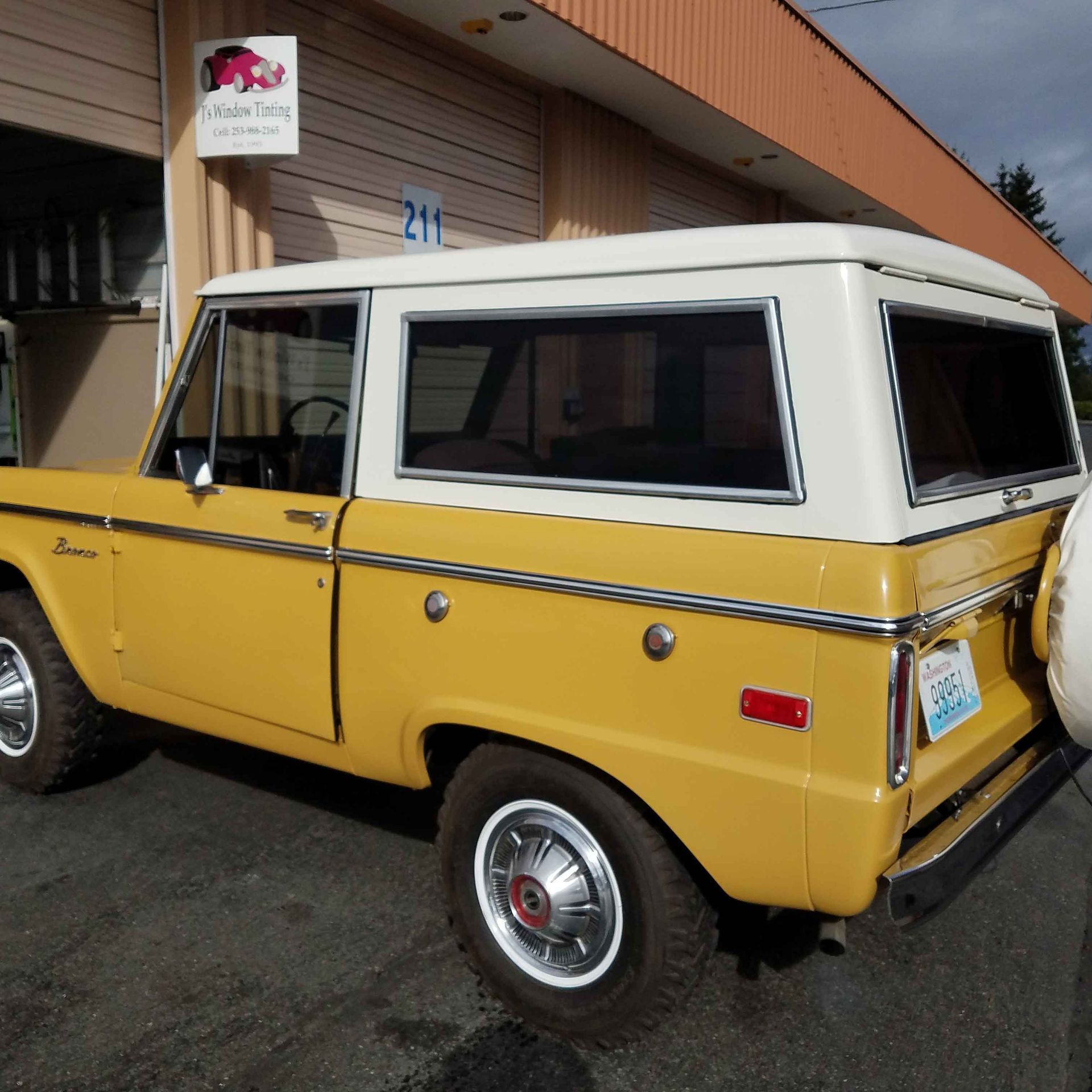 Yellow and white vintage Ford Bronco parked in front of a building.