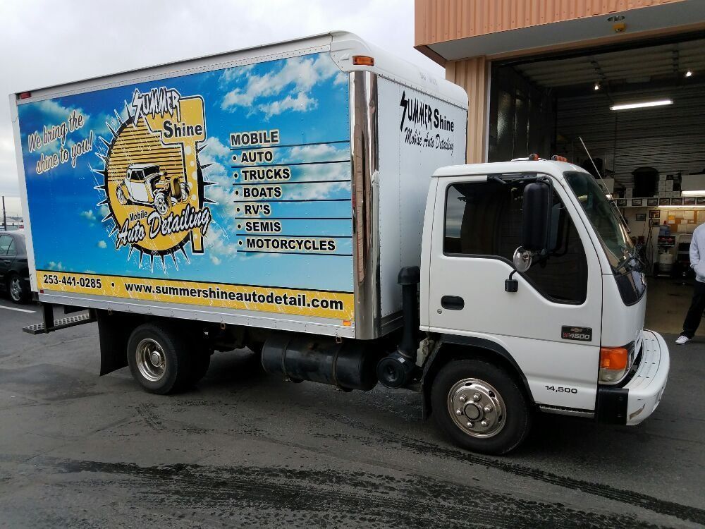 White box truck with blue and yellow logo for mobile detailing services parked outside.
