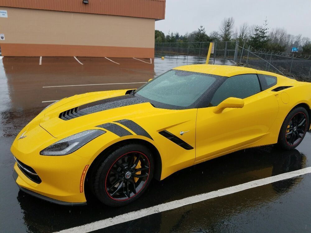 Yellow Corvette sports car with black accents parked on wet pavement.