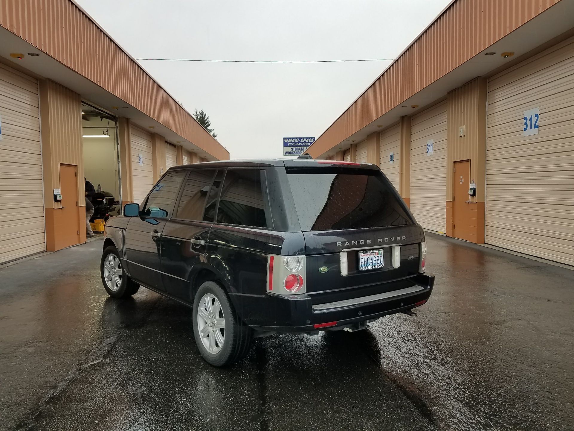 Black Range Rover SUV parked between rows of storage units on wet pavement.