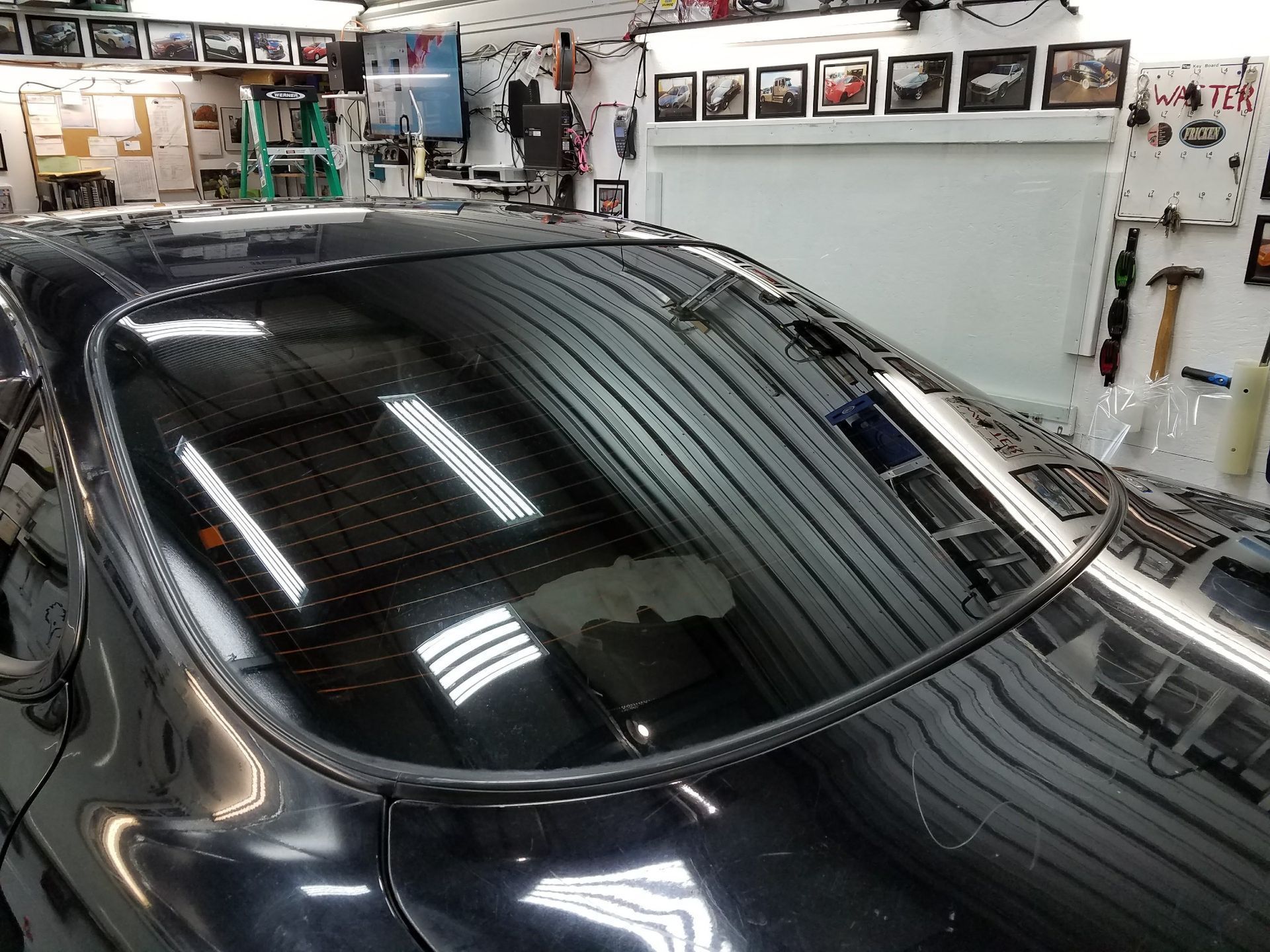Black car's rear window being worked on inside a garage.