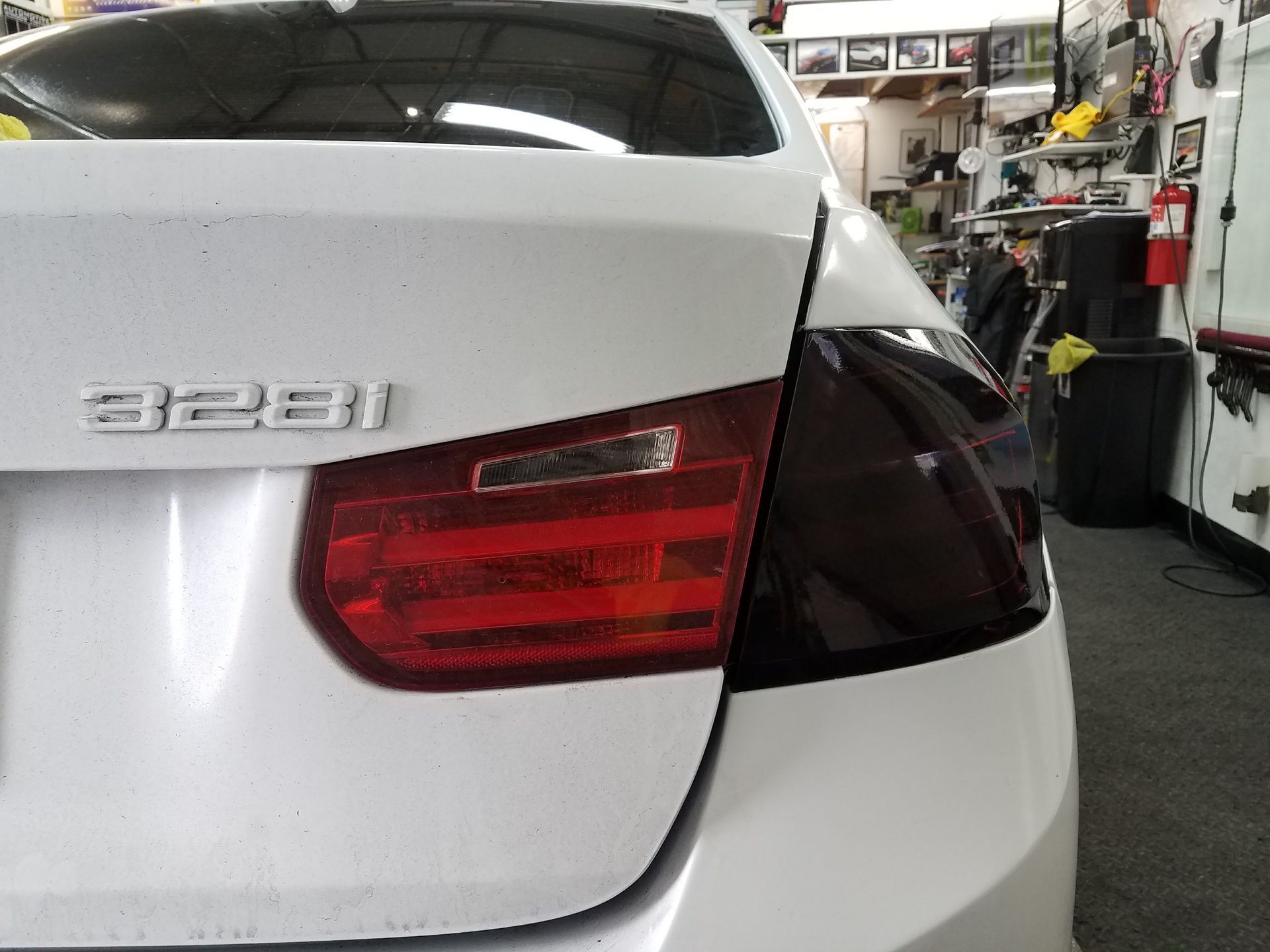 White BMW 328i rear with tinted taillights in a shop.