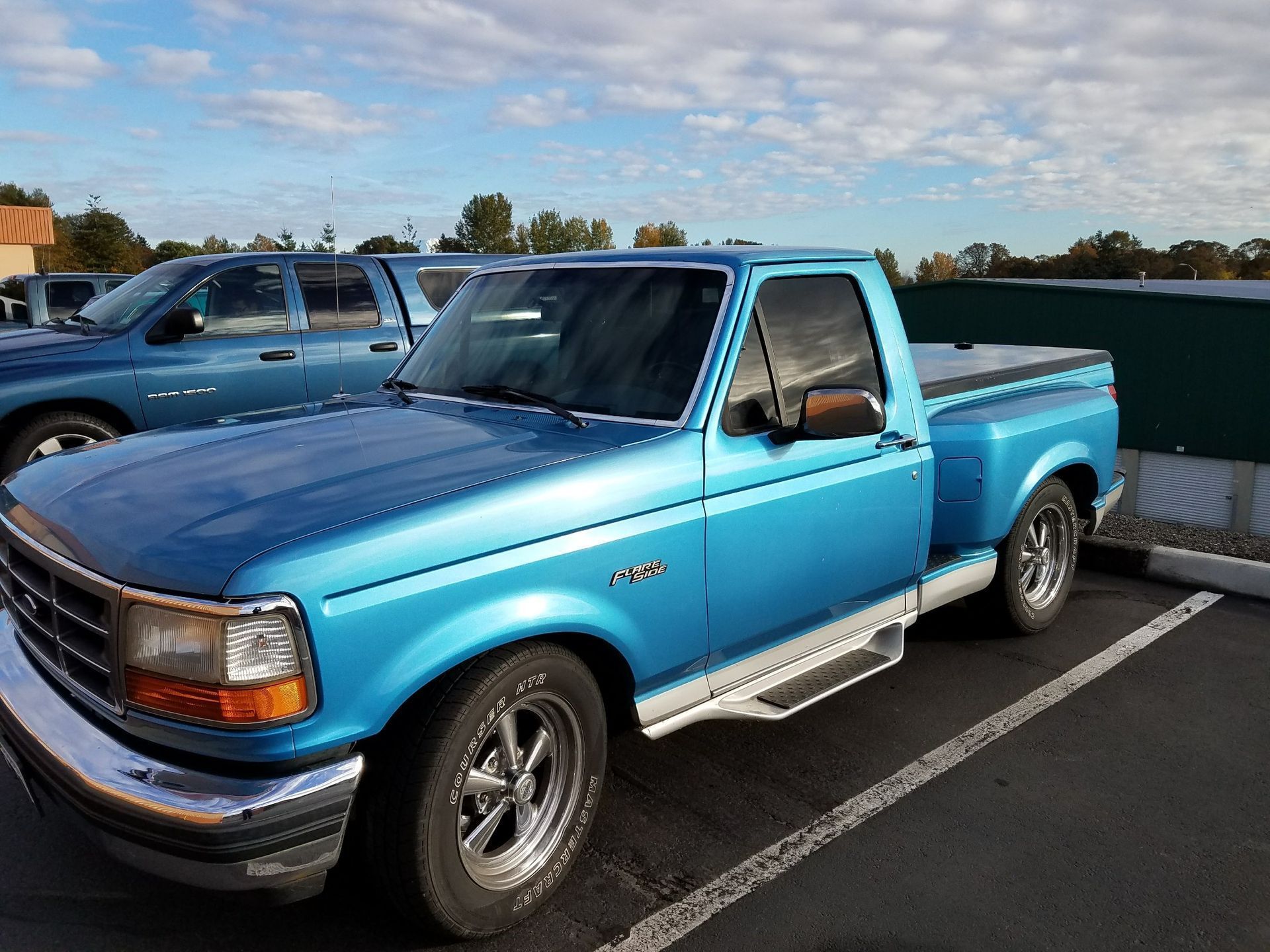 Blue Ford F-150 pickup truck parked in lot on a partly cloudy day.