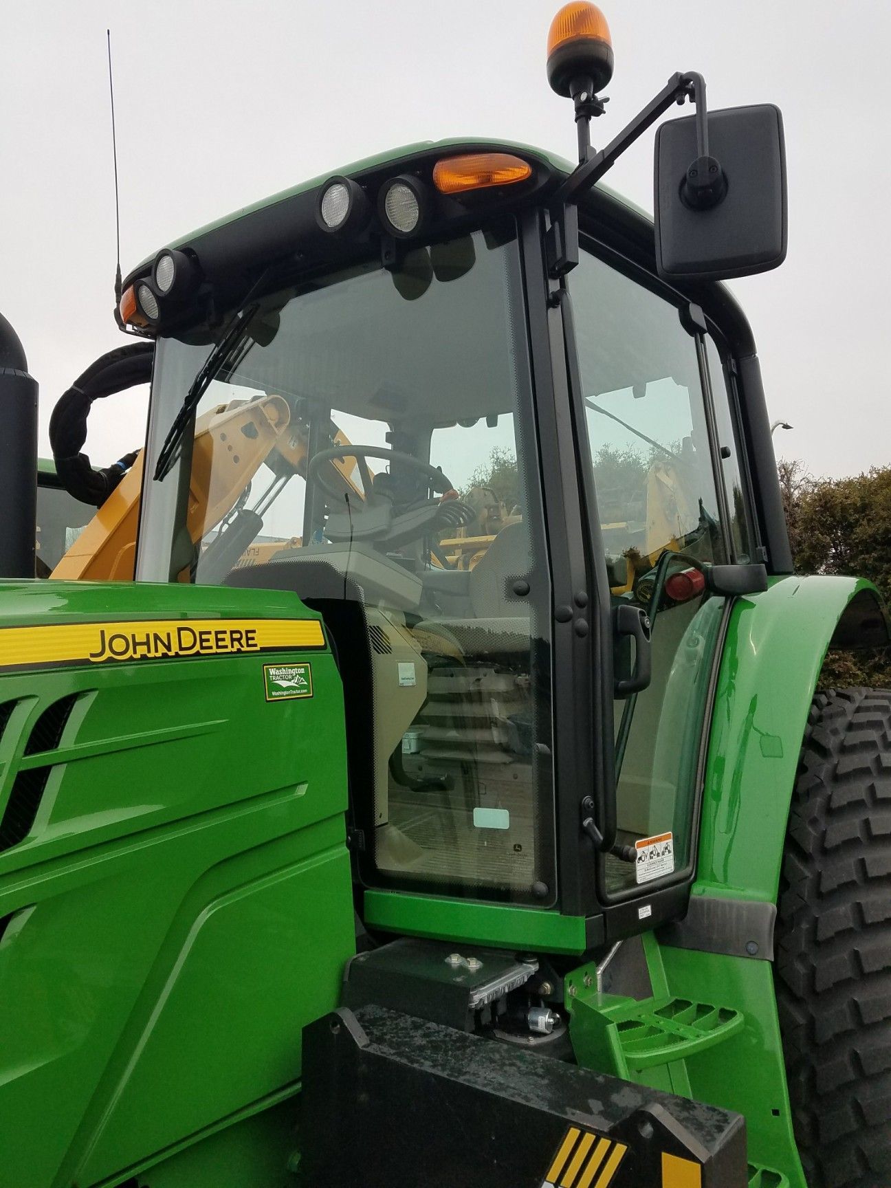 Green John Deere tractor cab, with lights, against a cloudy sky.