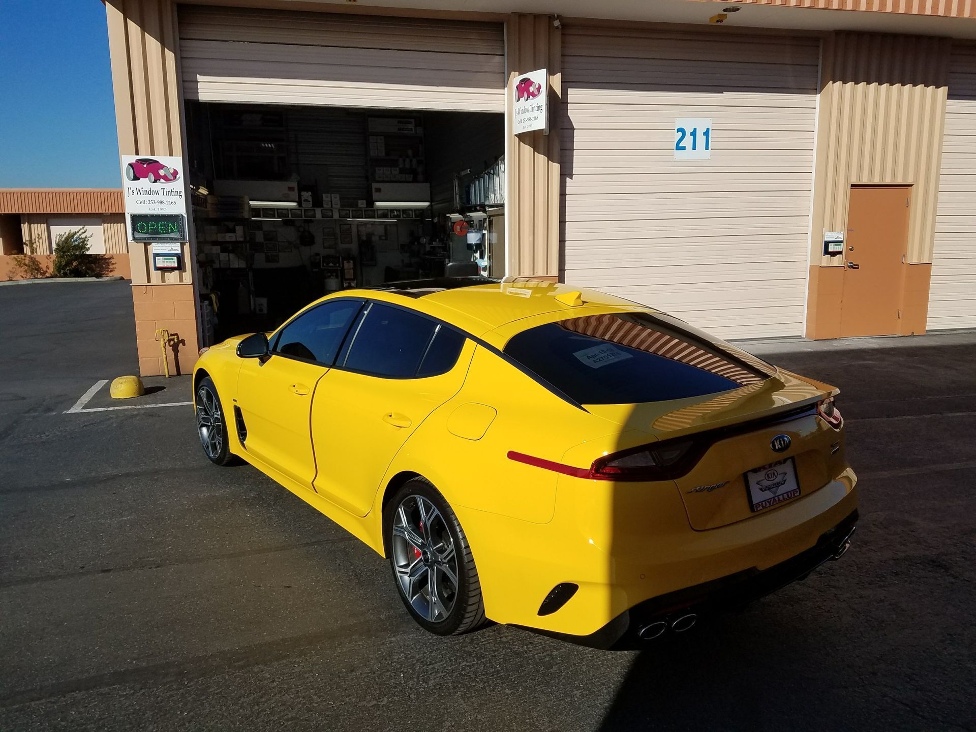 Yellow Kia Stinger parked in front of a garage with its door open.
