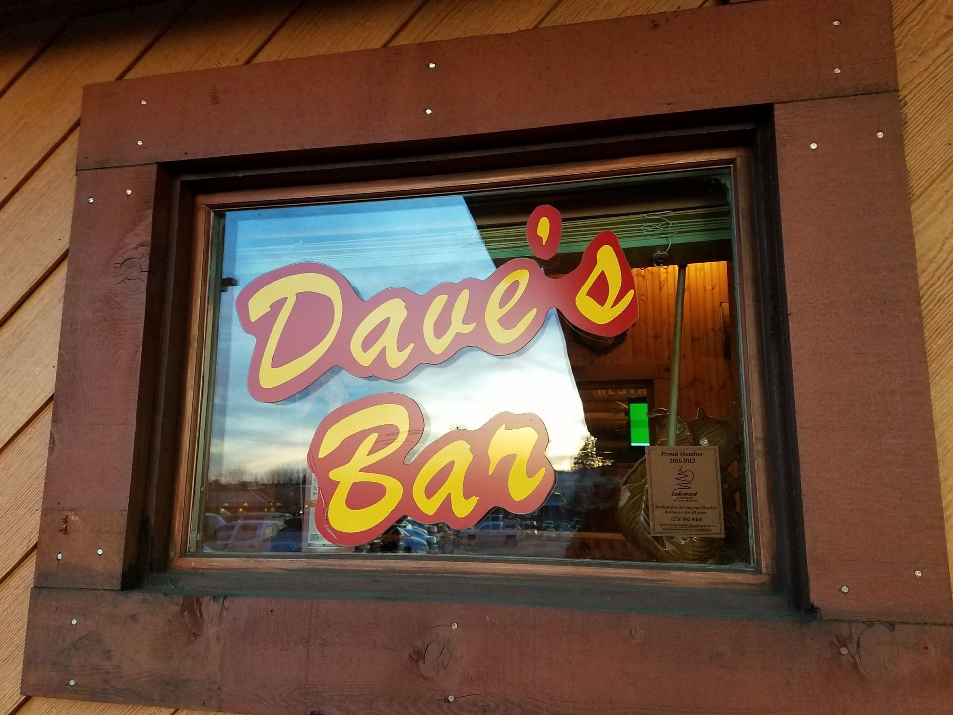 Dave's Bar sign in a window. Red and yellow text. Exterior view. Brown frame.