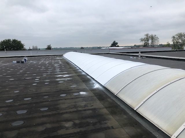 Een lang, gebogen dakraam bevindt zich in een plat, donker dak onder een bewolkte hemel.