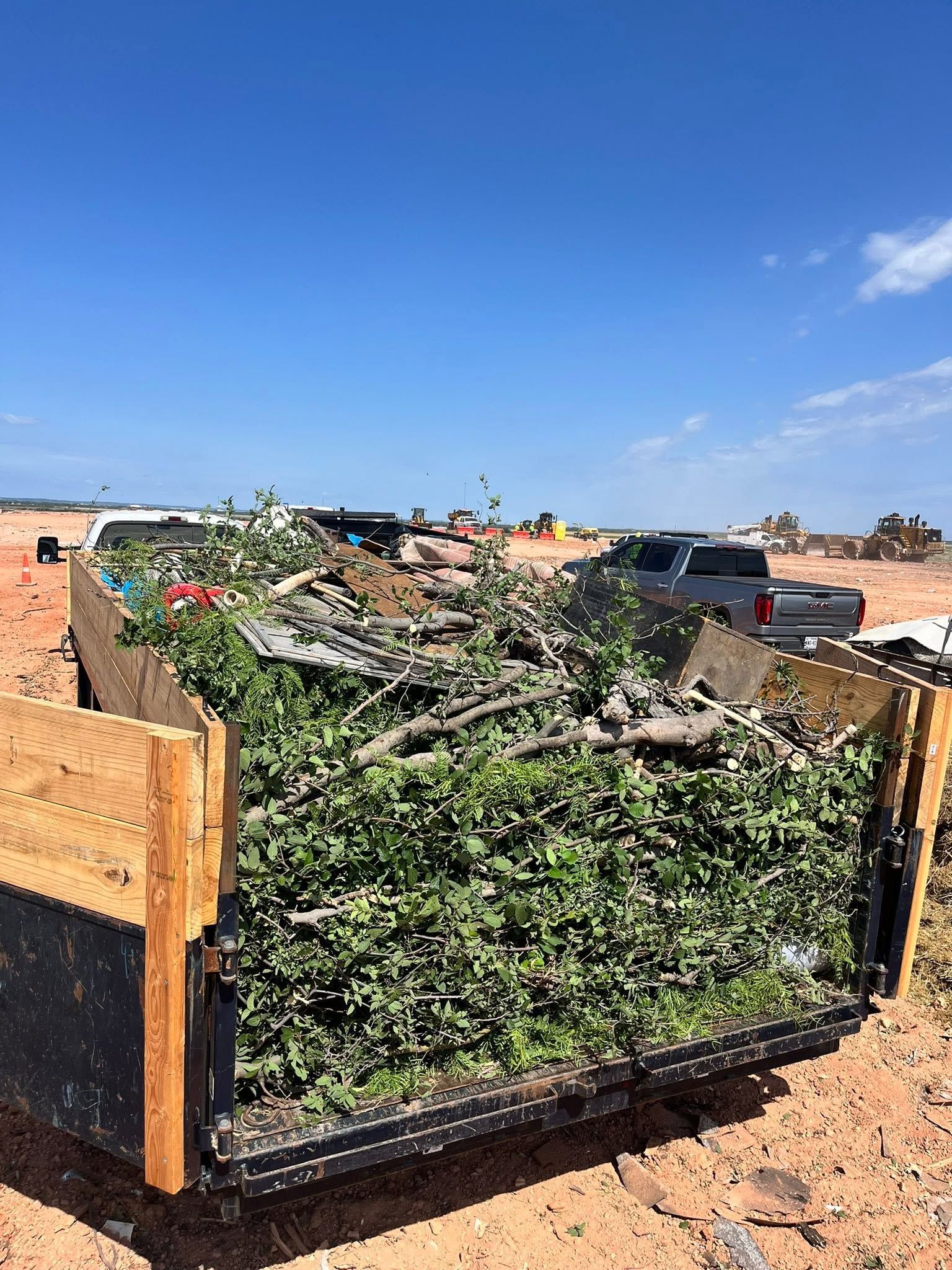 Raised garden bed filled with green vines and debris on a sunny day, with a blue sky overhead