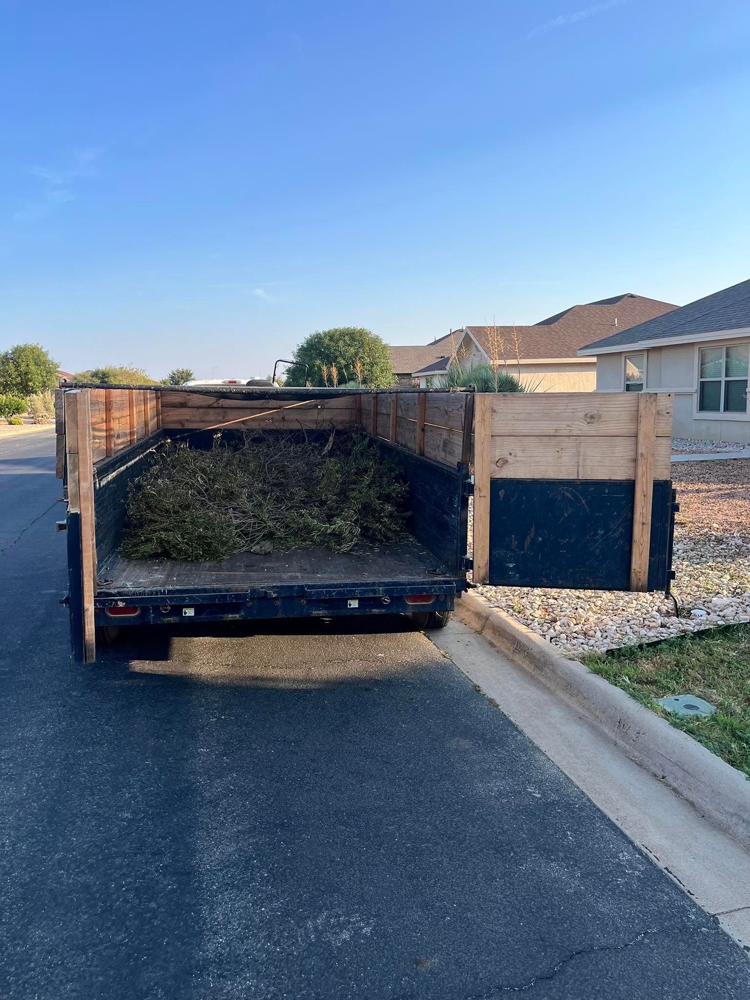 Loaded black utility trailer parked by a curb in a residential driveway