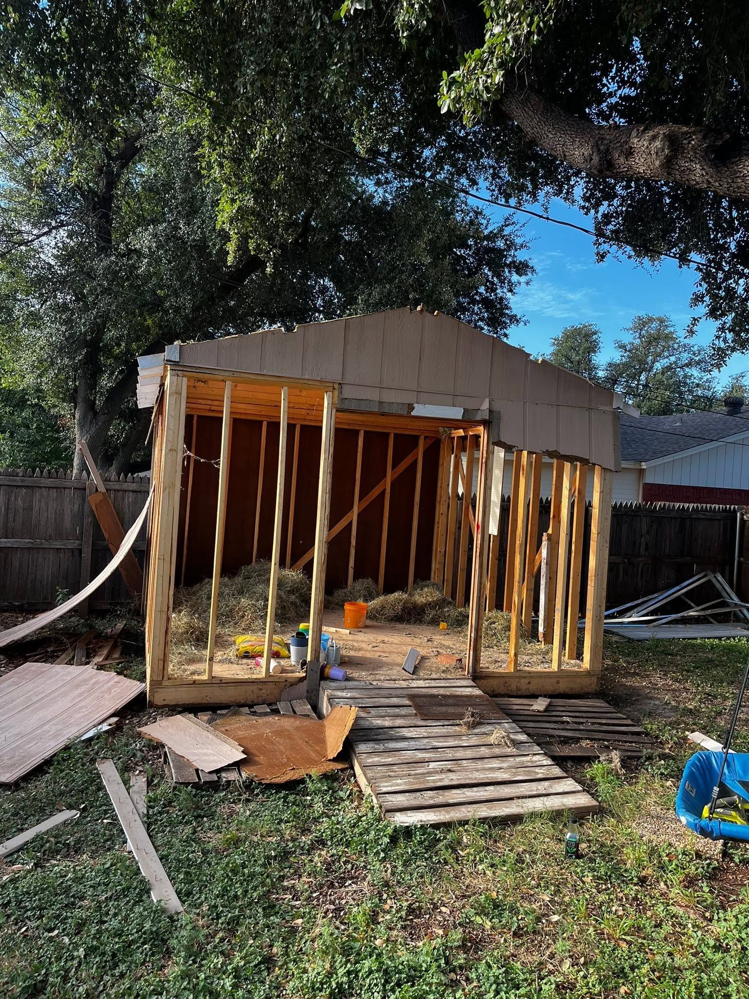 Partially built wooden shed frame in a backyard, with exposed studs and debris on the ground.
