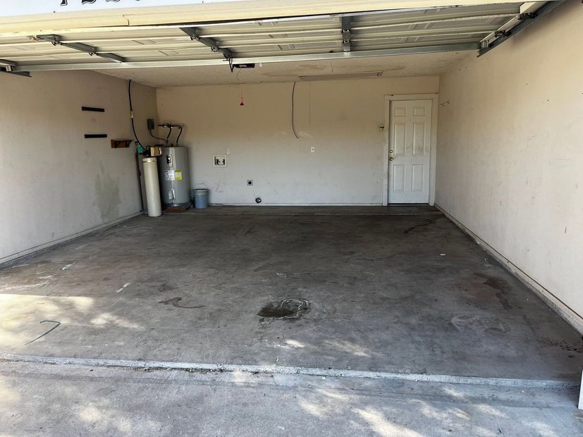 Empty garage with concrete floor, white walls, a closed door, and gas cylinders along the left wall.