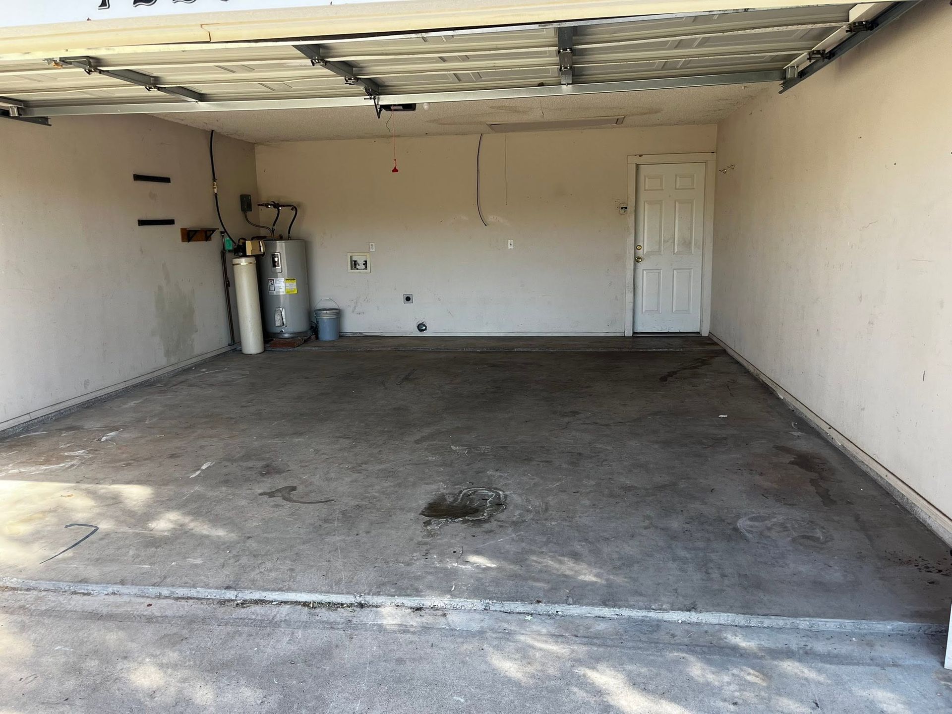 Empty garage interior with concrete floor, white walls, ceiling damage, and gas cylinders in the back left corner