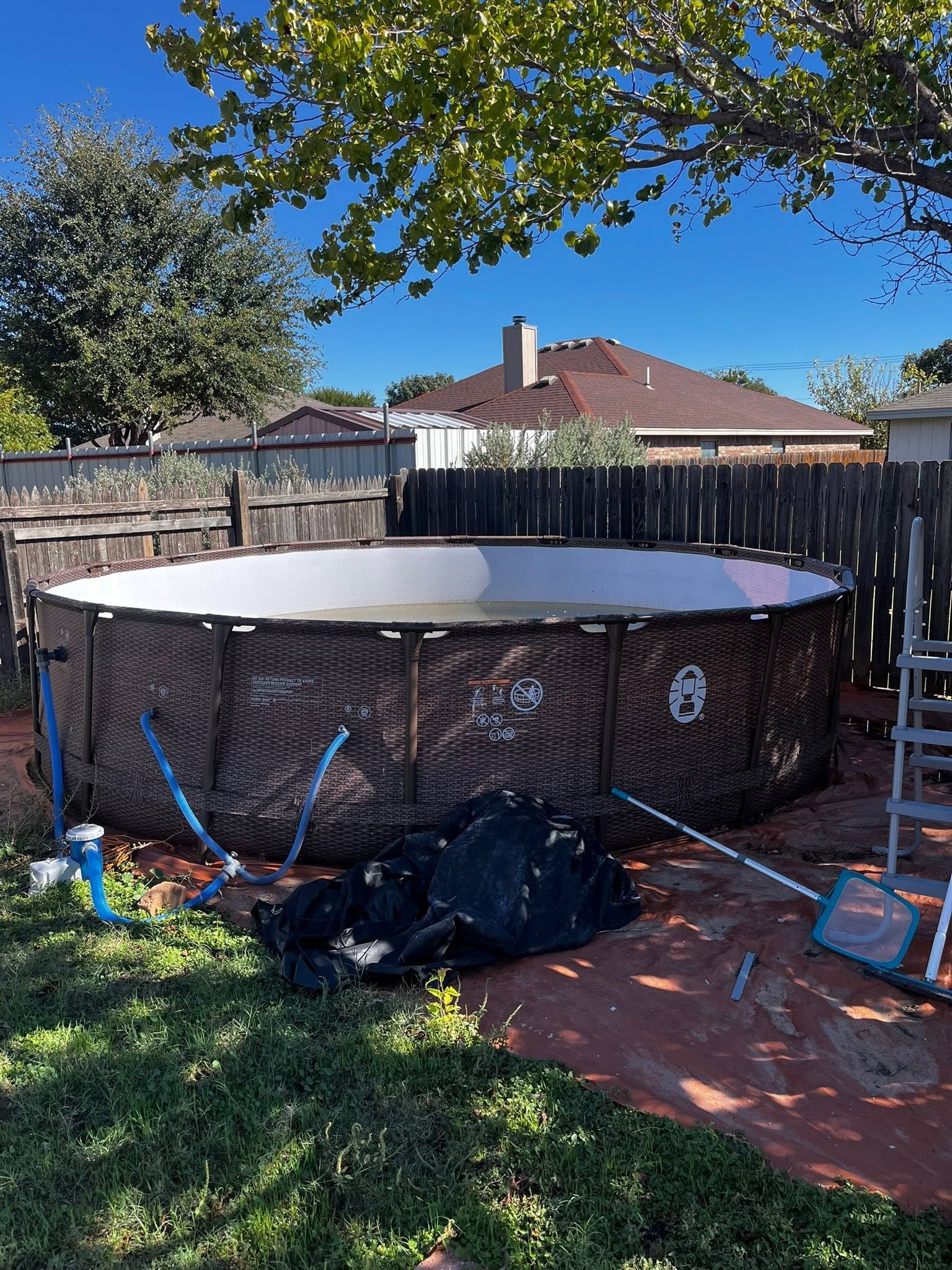 Backyard above-ground pool with wooden sides and a fence, under a tree on a sunny day