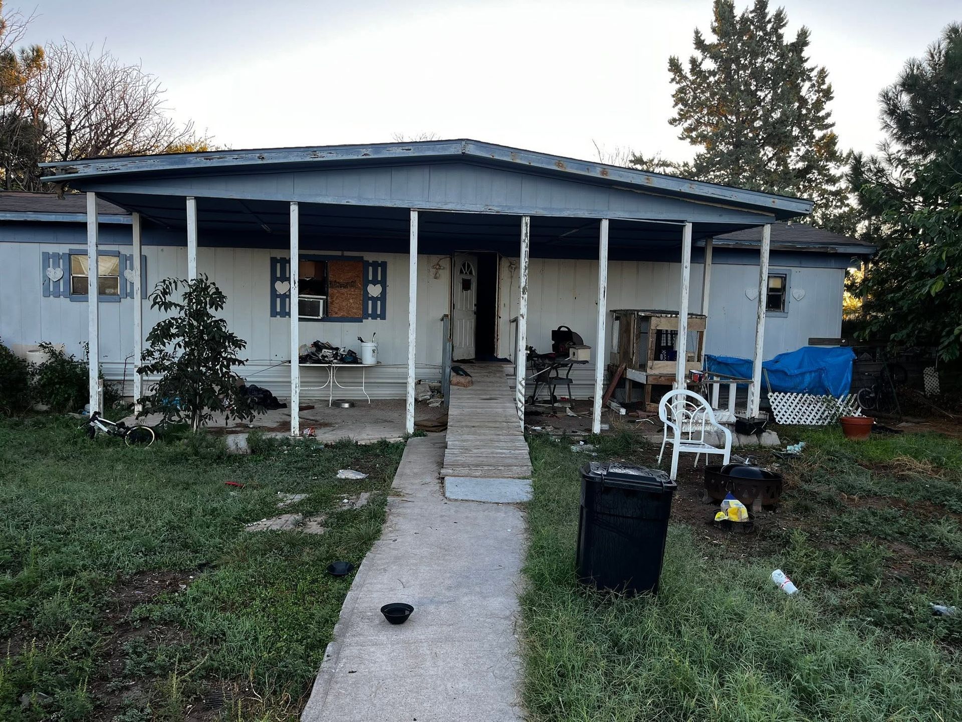 Small house with a covered porch, centered walkway, and scattered outdoor items in the front yard.
