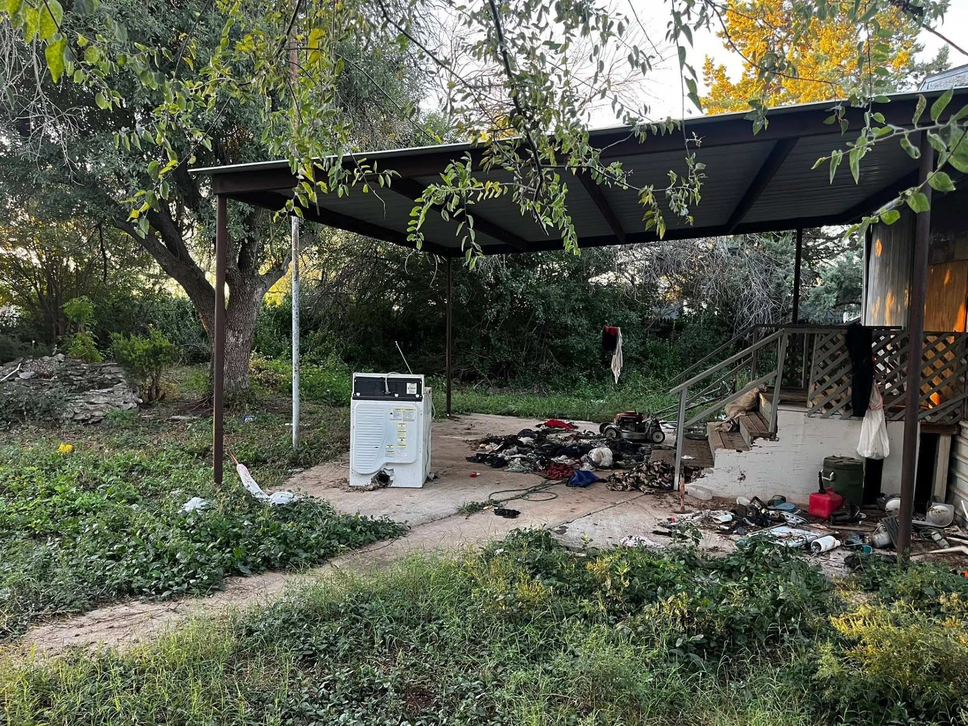 Outdoor patio with a black canopy, scattered tools, and a portable air conditioner under trees