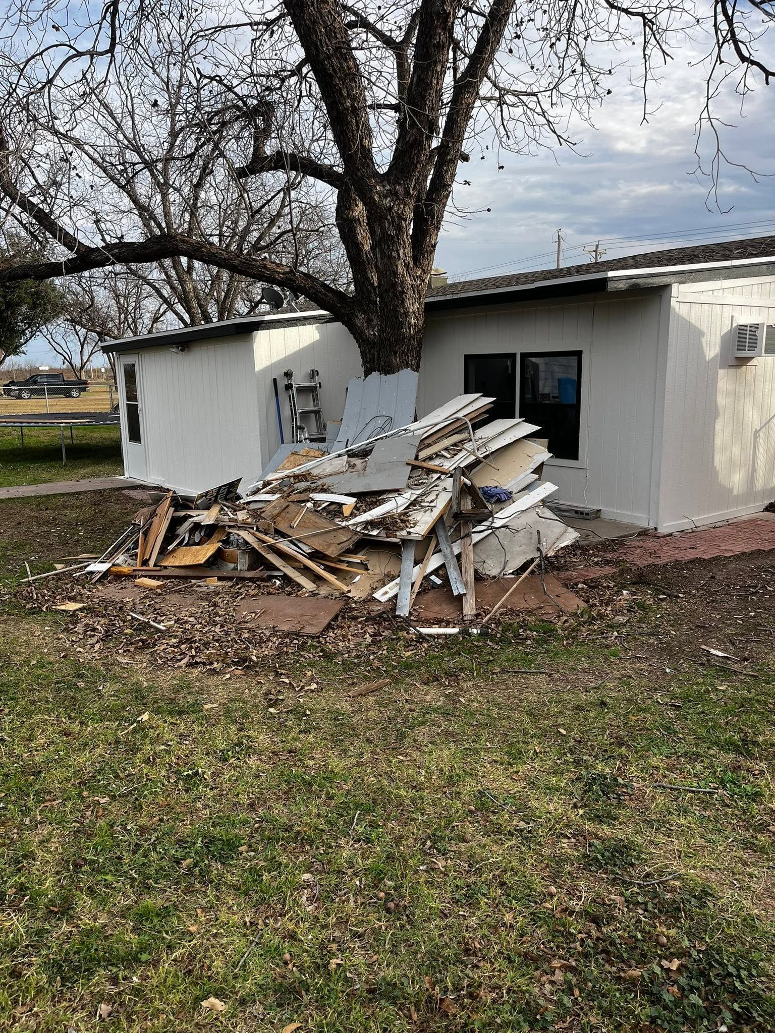 Pile of building debris beside a white house under a large tree in a yard