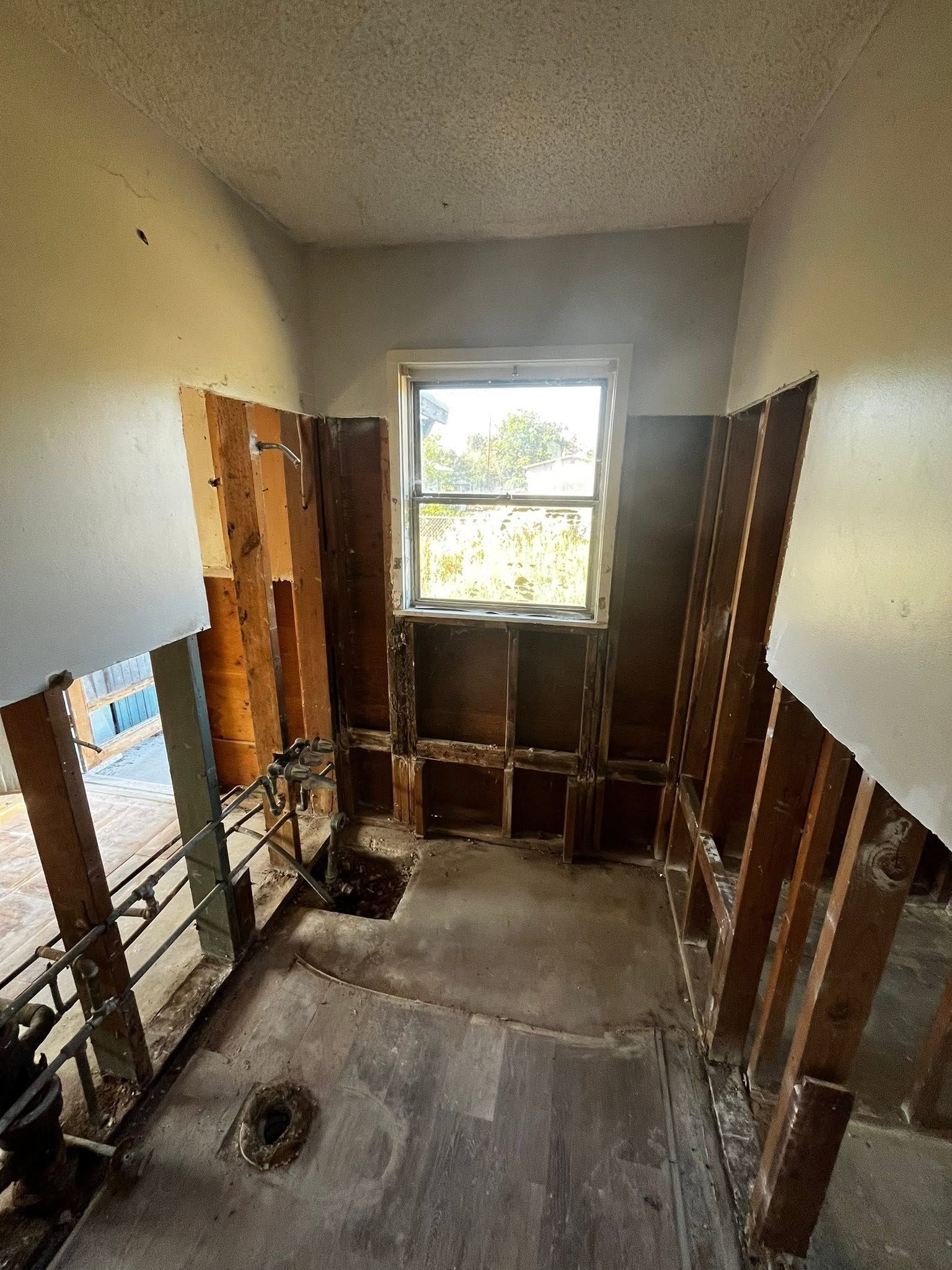 Bare room under renovation with exposed studs, a window, and debris on the floor