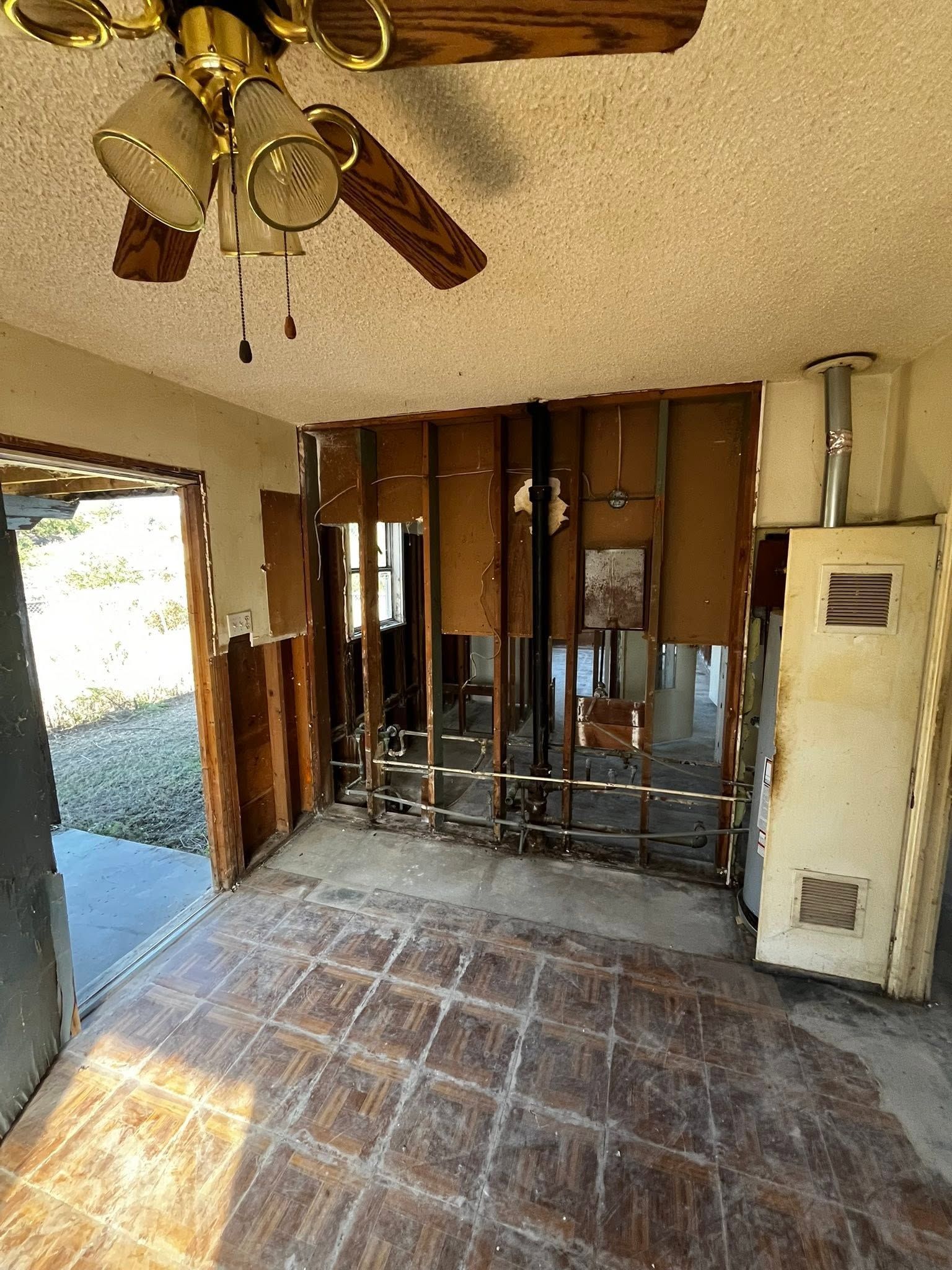 Damaged interior room with exposed studs, debris, and a ceiling fan; open doorway to outside.