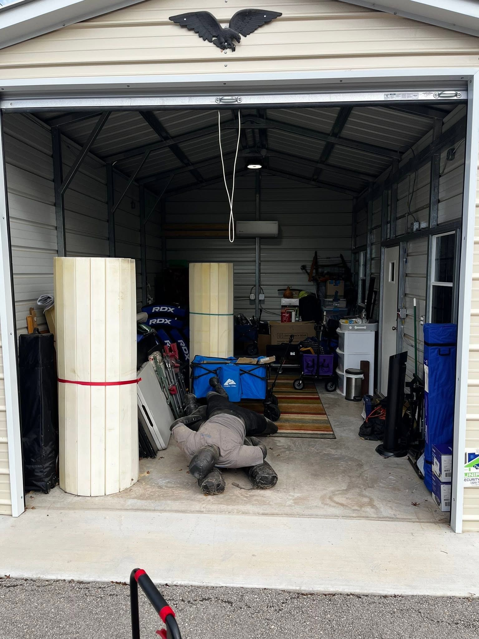 Open garage filled with tools, equipment, and large rolled white material near the entrance.