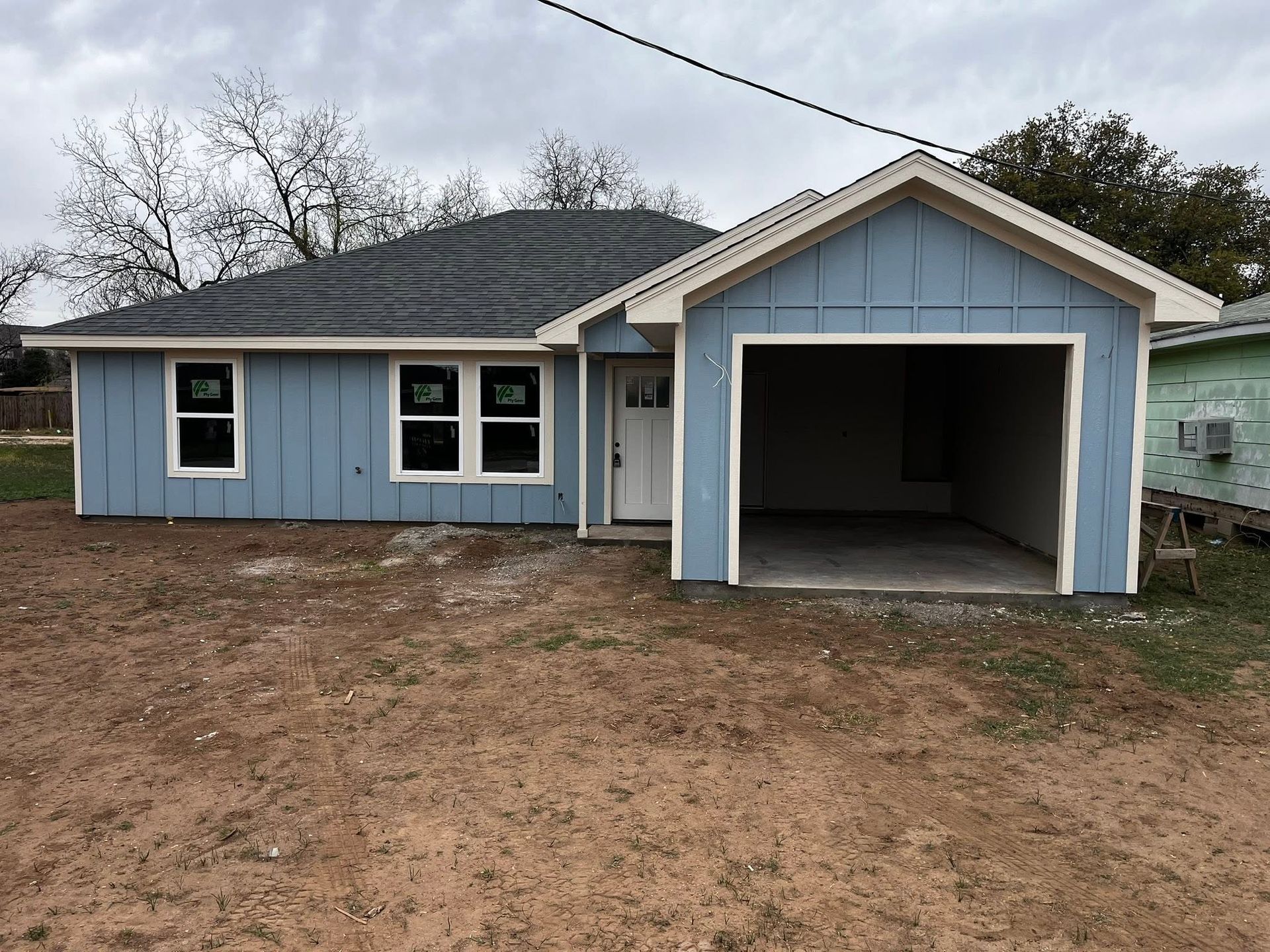 Light blue house with attached garage and dirt front yard under cloudy sky