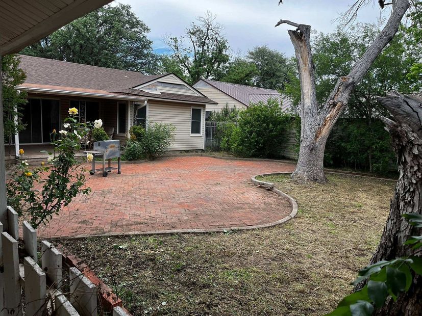 Small backyard with a patio, brick patio edge, lawn, trees, and a single-story house.