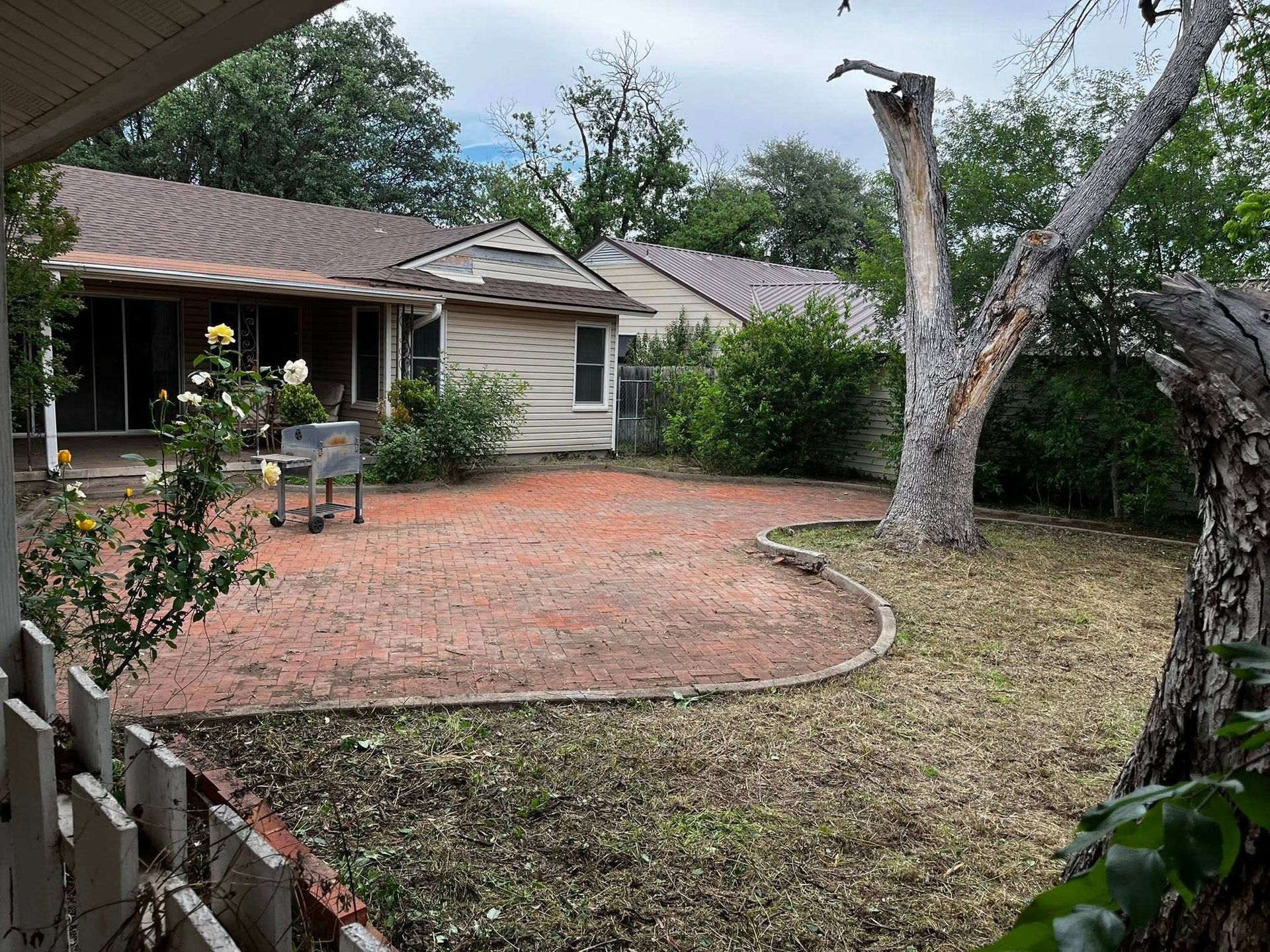 Backyard with brick patio, small house, large tree, and wooden fence on the left