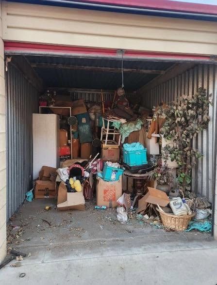 Open storage unit packed with boxes, baskets, furniture and household clutter.