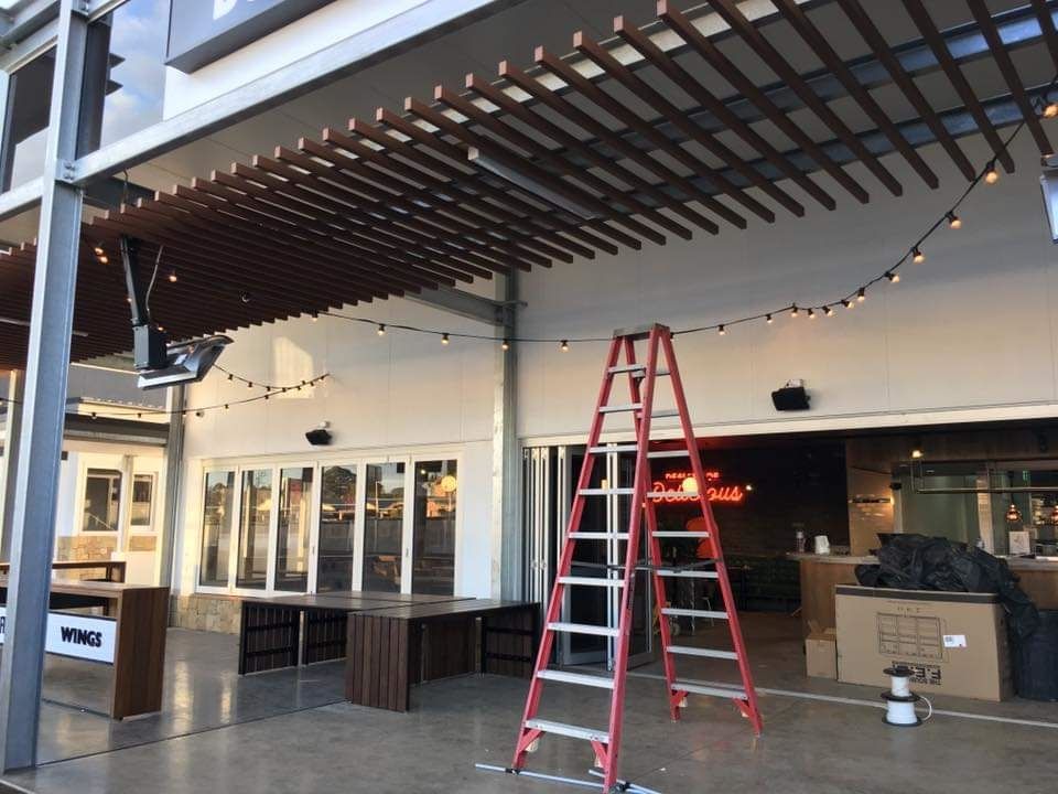 A Tall Red Stepladder Stands on A Concrete Patio Under a Wooden Slatted Roof — AC/DC Electrical, Air Conditioning & Refrigeration In Zilzie, QLD
