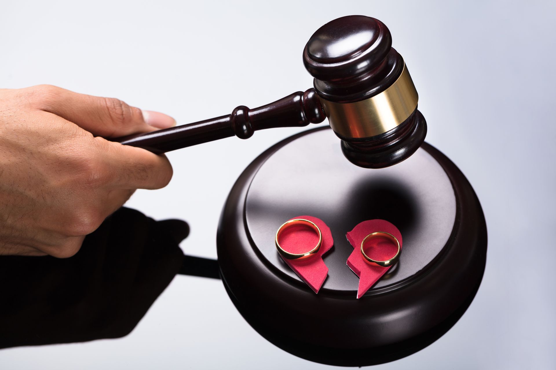 Hand holding gavel over broken heart and wedding rings on sounding block.
