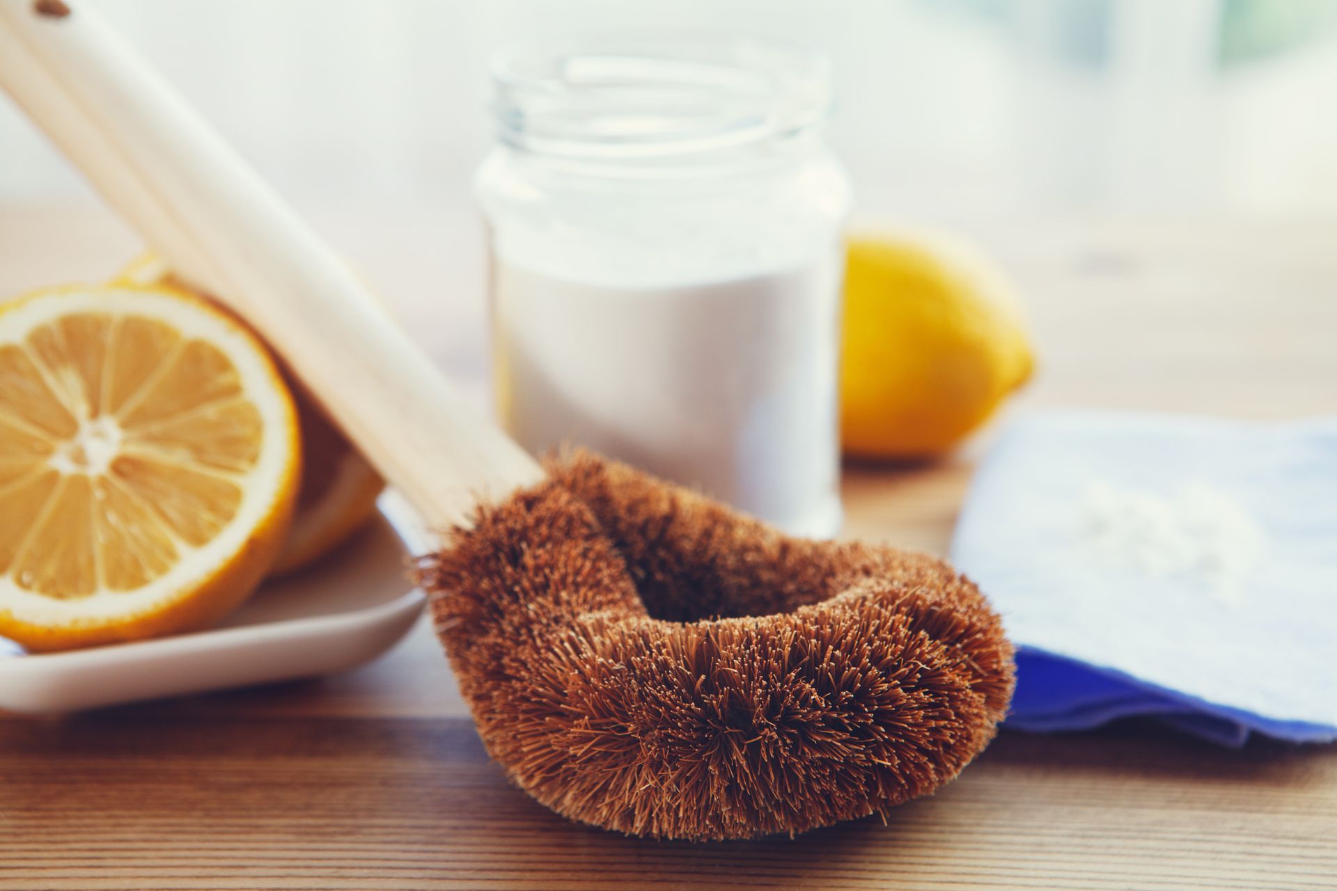 A wooden brush is sitting on a wooden table next to lemons and baking soda.