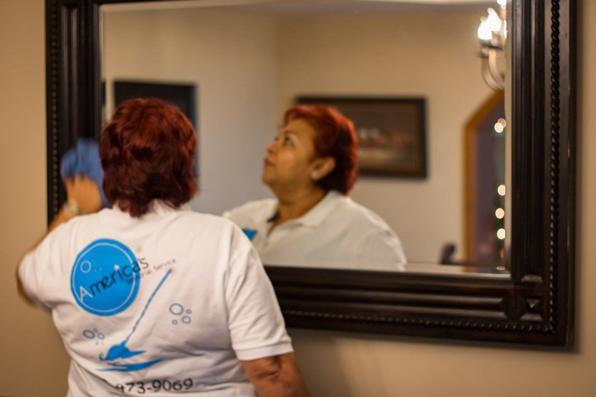 Person in white shirt looking at their reflection in a bathroom mirror, seen from behind.