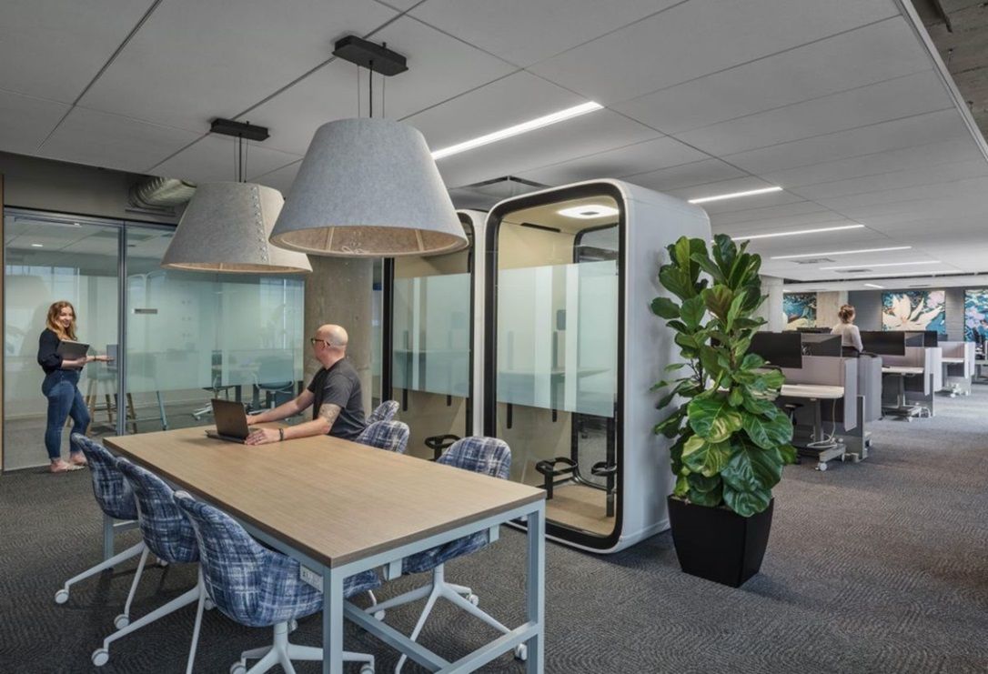 A man is sitting at a table in an office with a laptop.