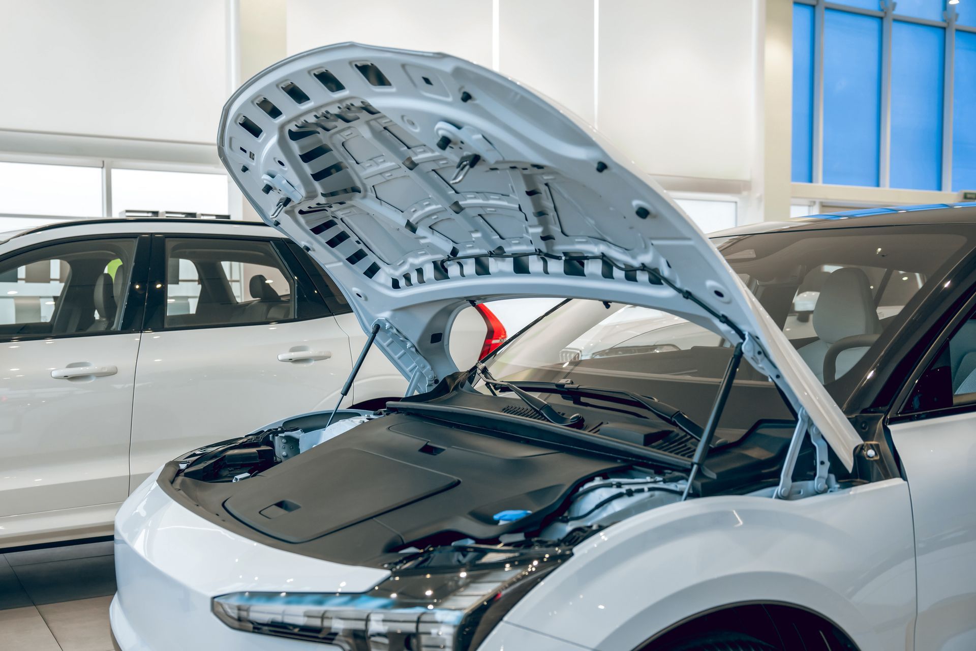 White SUV in a showroom with its hood open, revealing the engine bay.