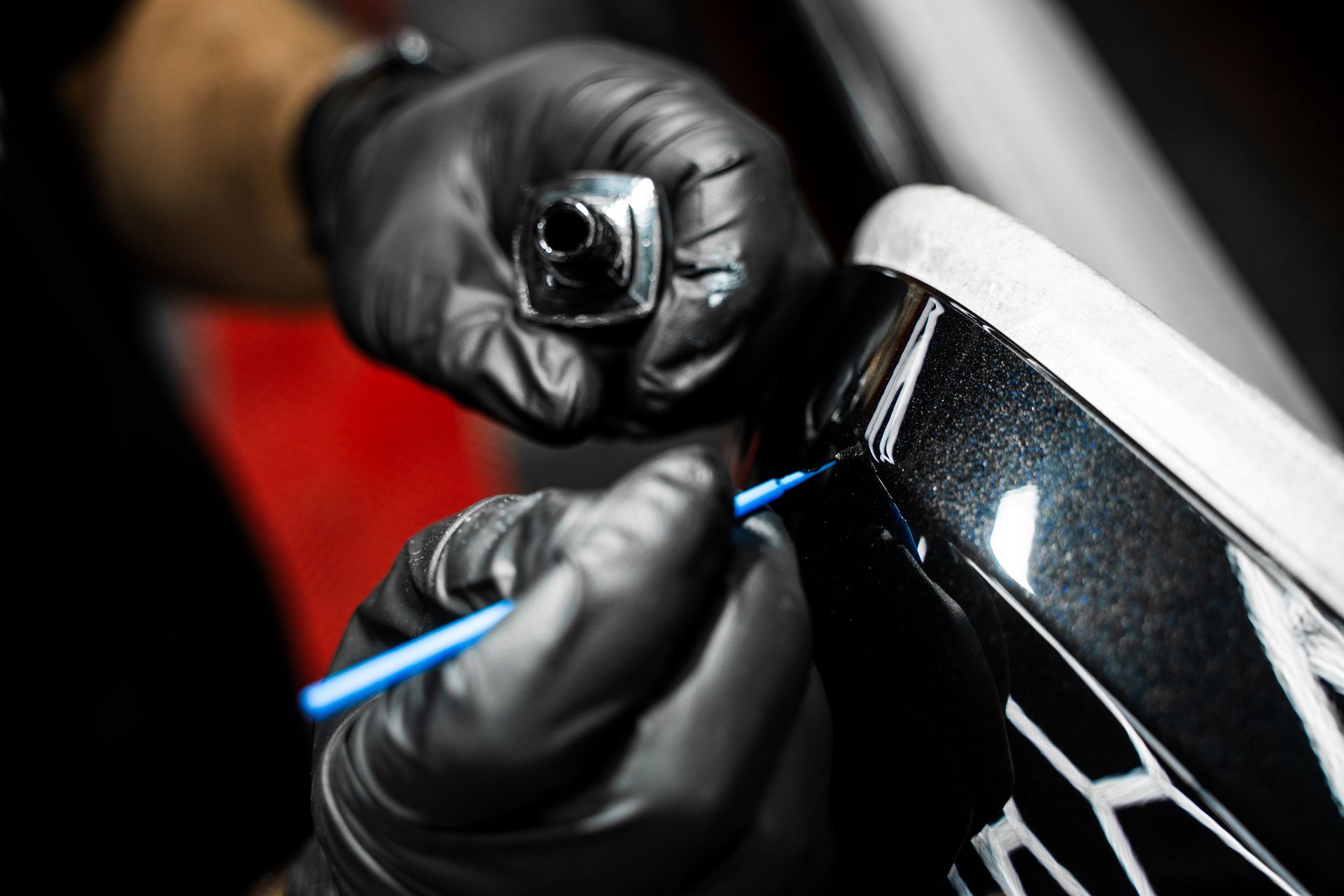 Gloved hands detailing a black car panel with a blue tool and a polishing cloth