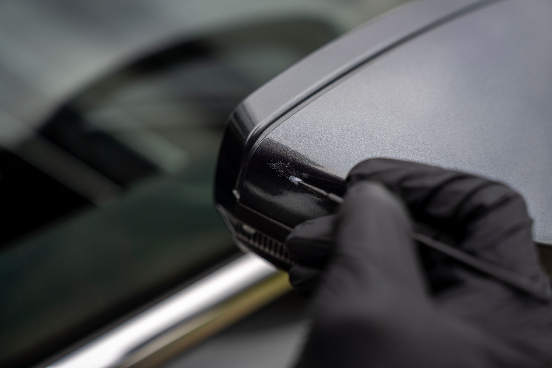 Gloved hand polishing a black car side mirror close-up