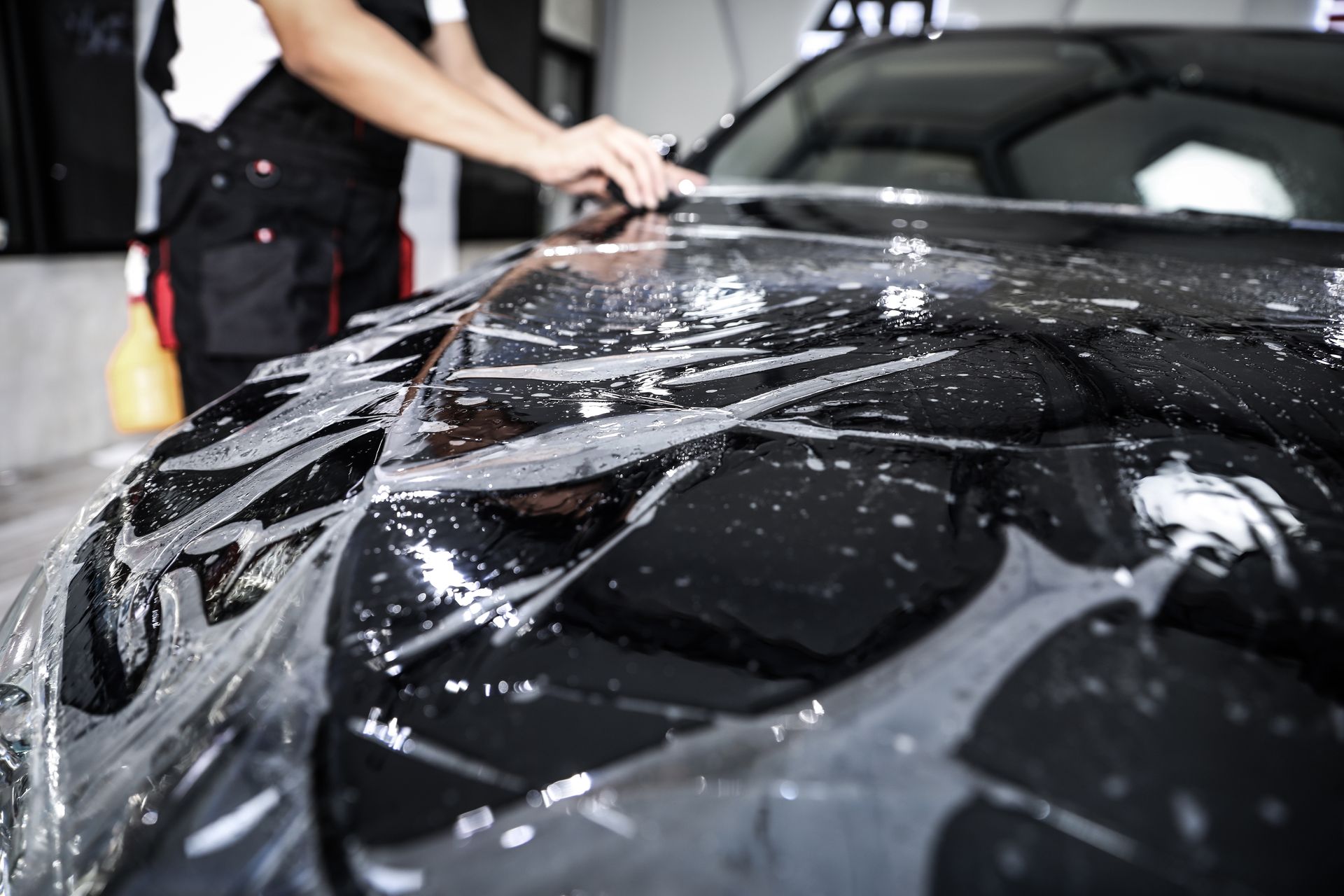 Car being wrapped with black glossy protective film in an auto shop