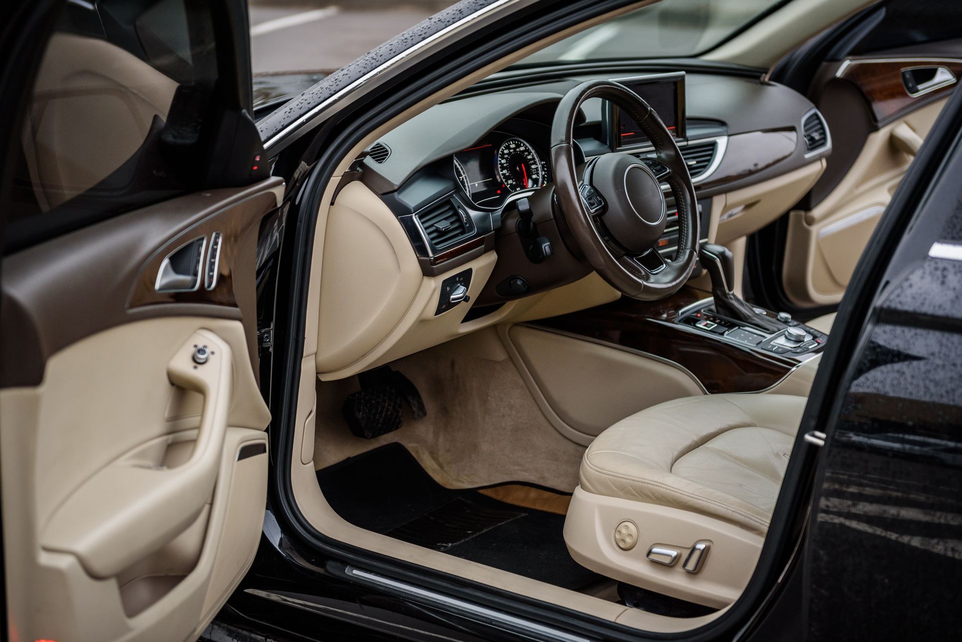 Luxury car interior with beige leather seats and wood trim, viewed through the open driver’s door