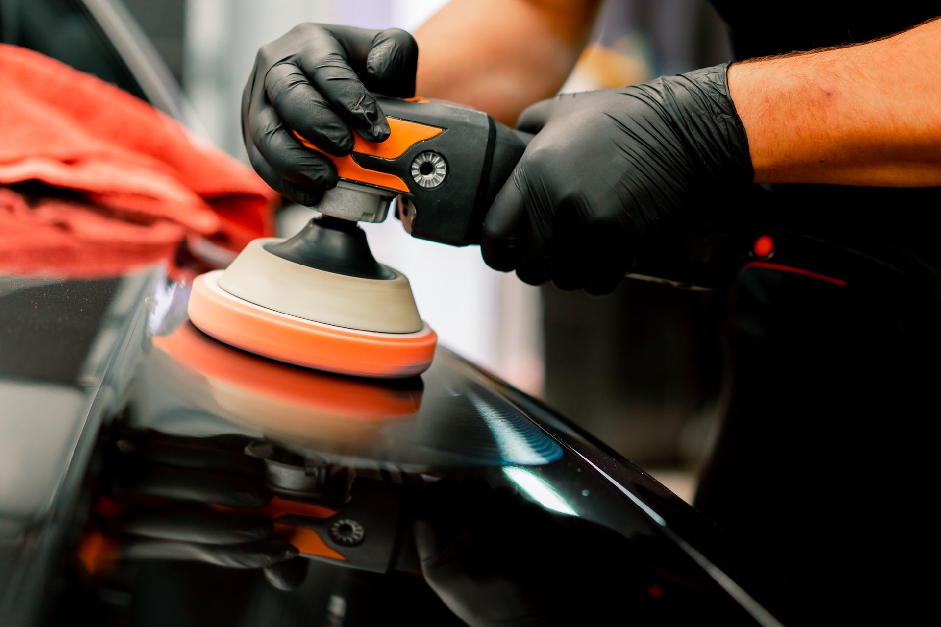Gloved hands polishing a black car with an orange buffer pad