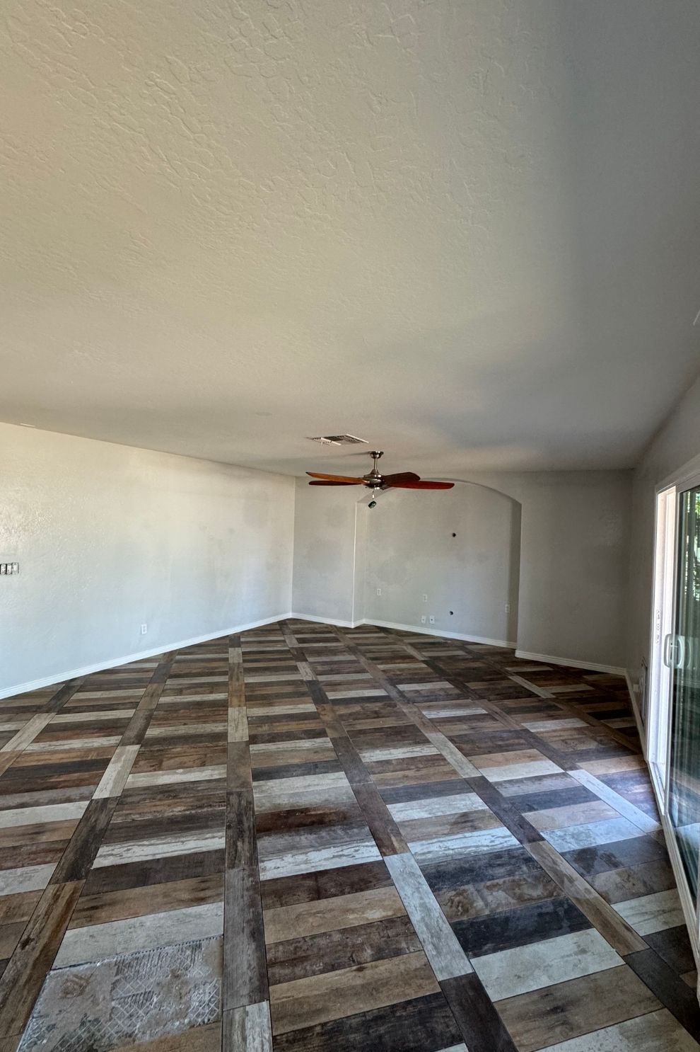 A large empty room with a wooden floor and a ceiling fan.