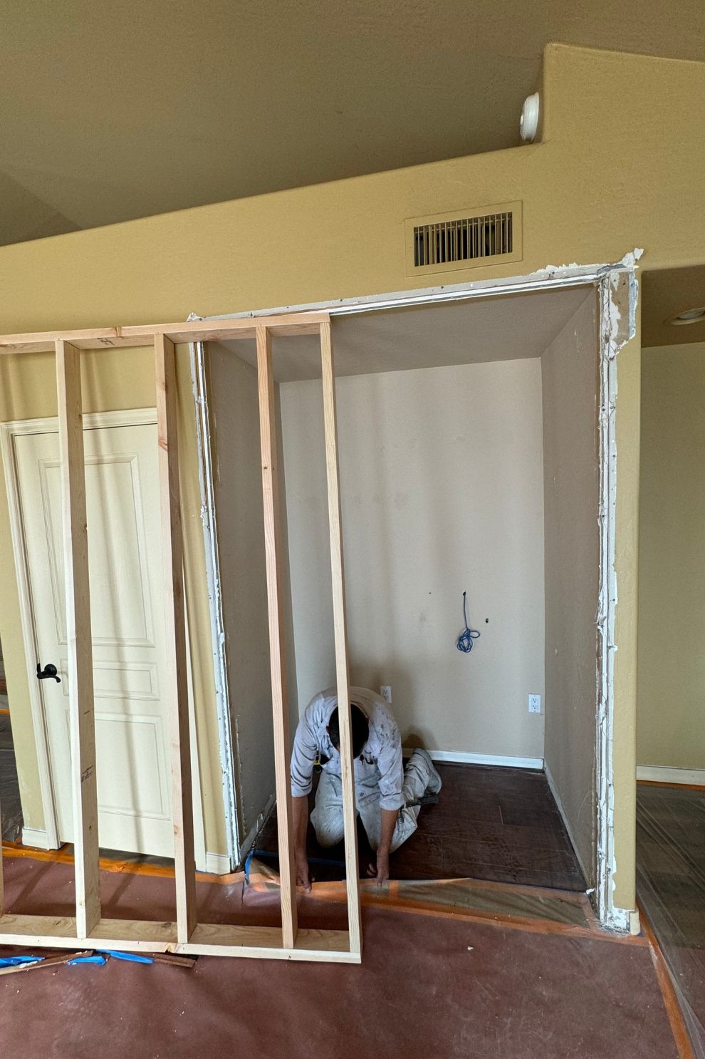 A man is kneeling in a room with a wooden frame.