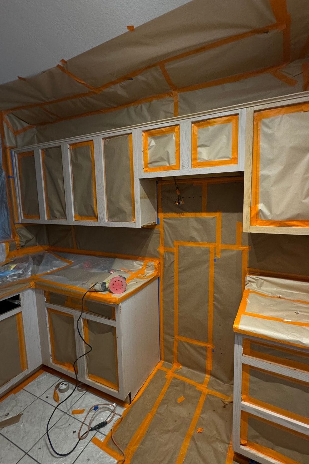A kitchen is being painted with orange and white tape.