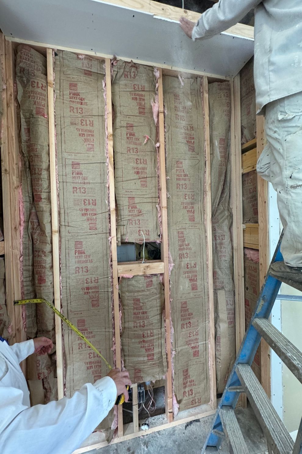 Two men are measuring a wall with a tape measure.