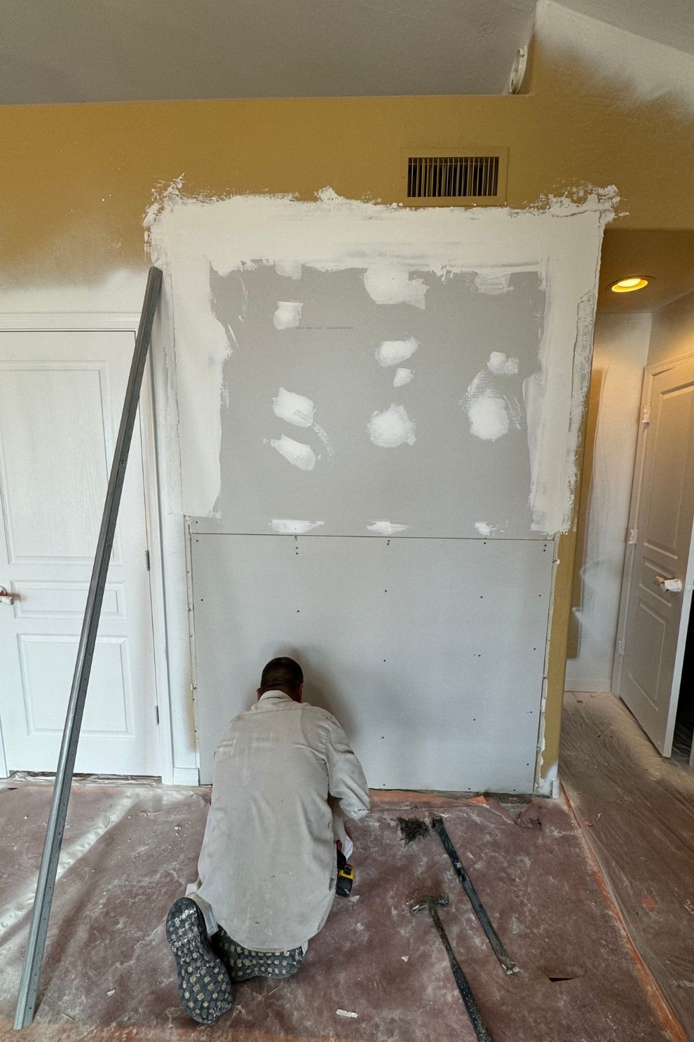 A man is kneeling down in front of a wall while painting it.
