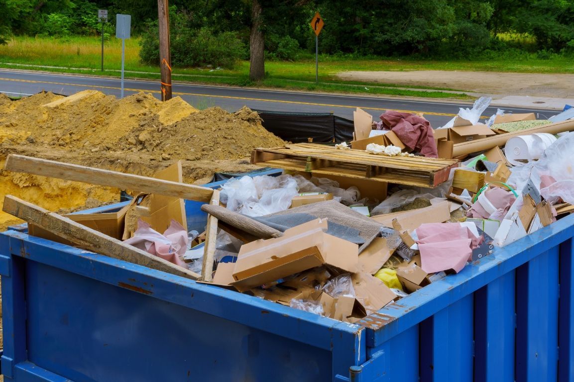 A blue dumpster filled with a lot of trash on the side of the road.